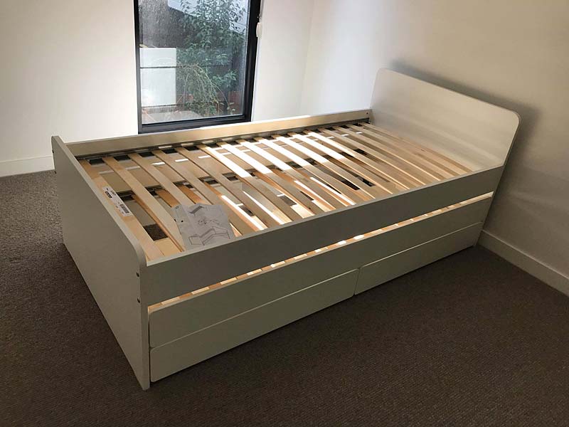 White wooden bed frame with slats and storage drawers assembled in a bedroom