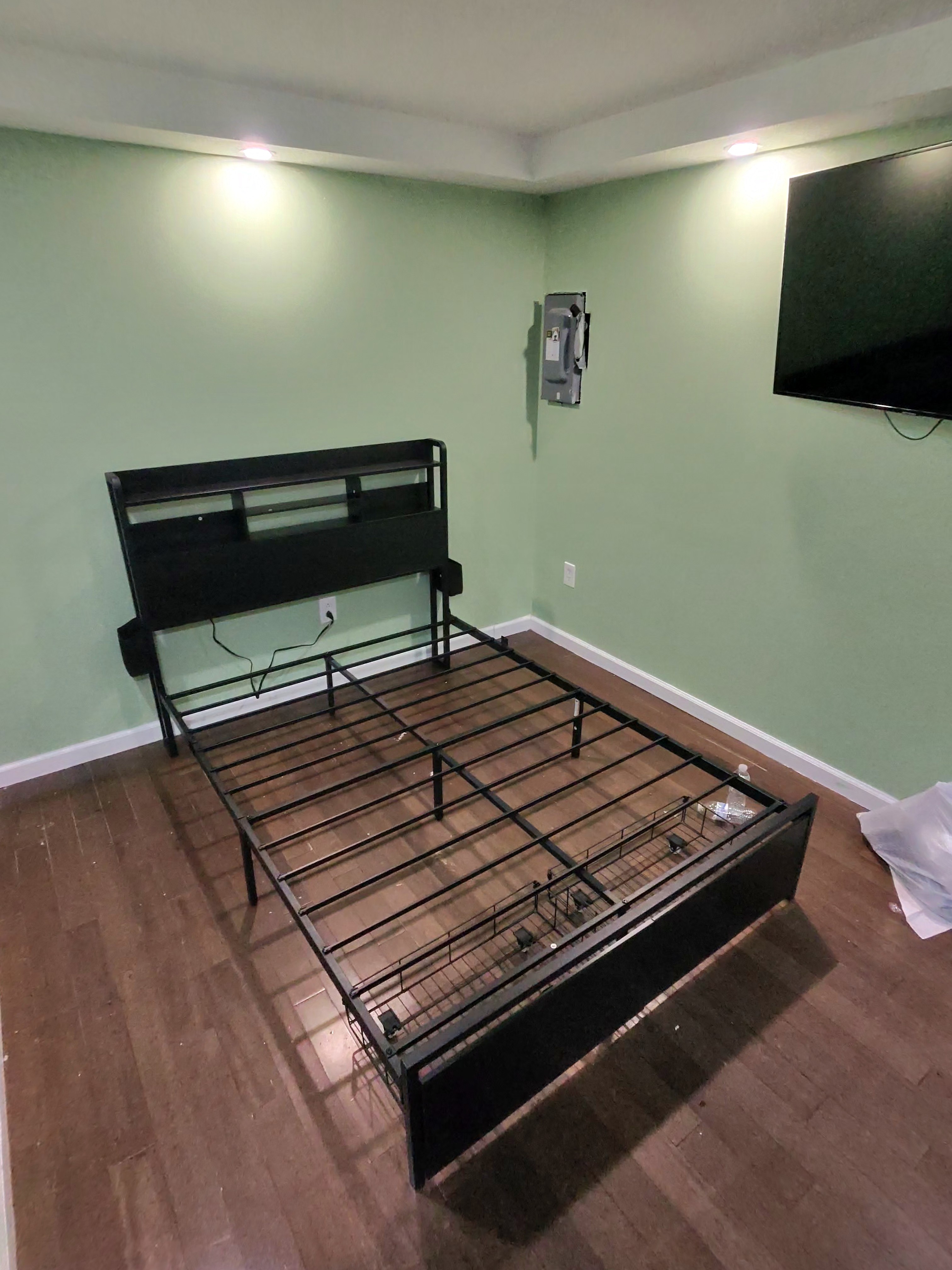 Assembled metal platform bed frame with bookcase headboard and a wall-mounted TV in a freshly finished bedroom